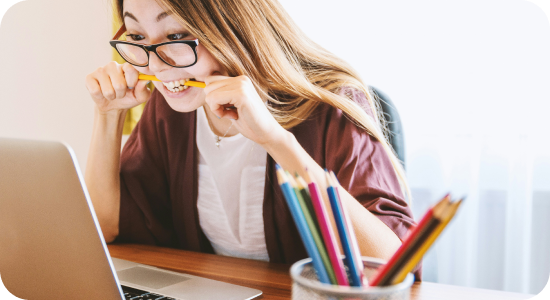 Girl biting a pen in front of a laptop